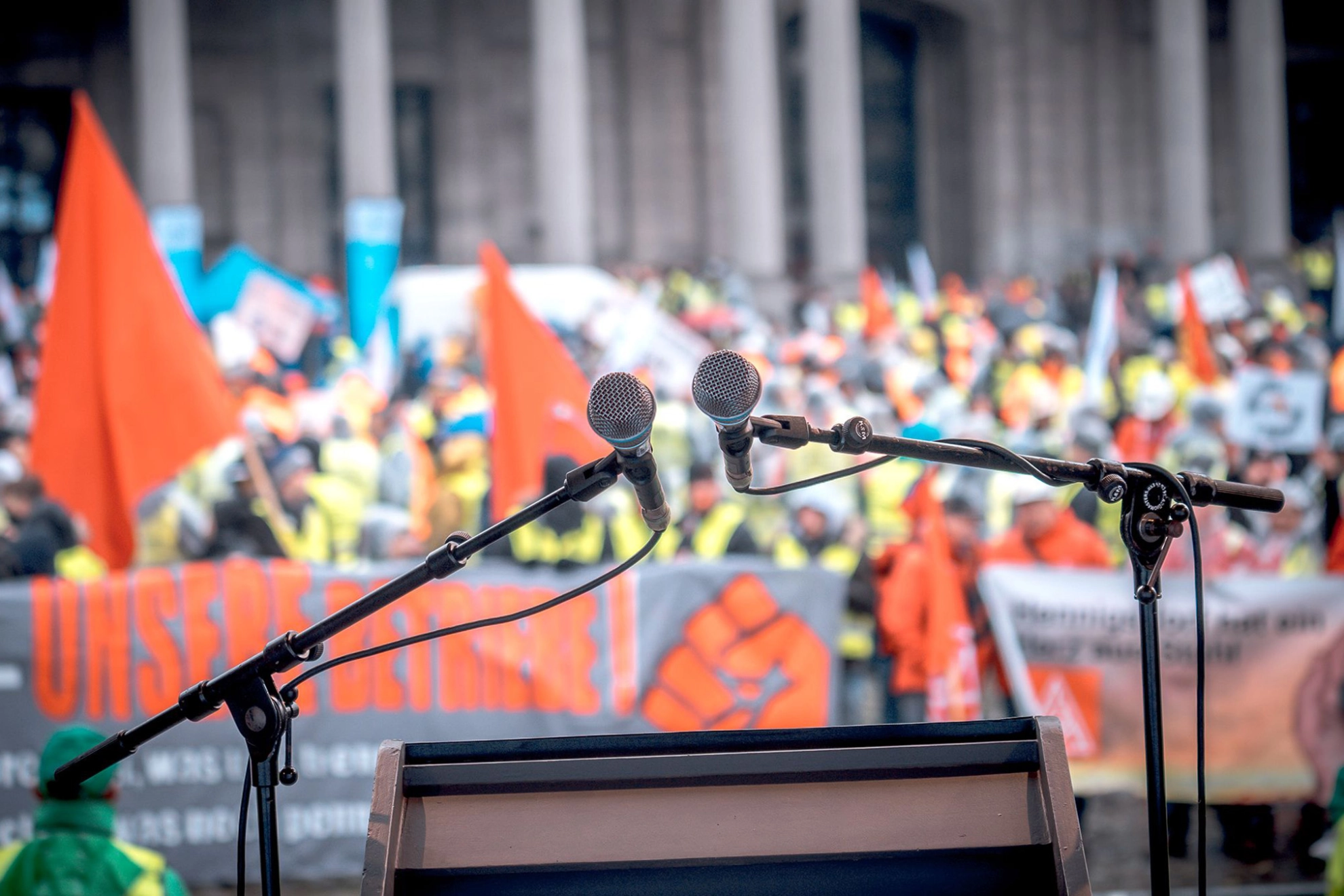 Zwei Mikrophone stehen auf einer Bühne vor einer Menschenmenge