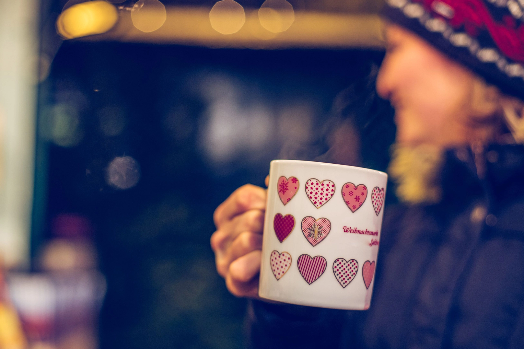 Eine Frau trinkt eine Tasse Glühwein auf einem Weihnachtsmarkt