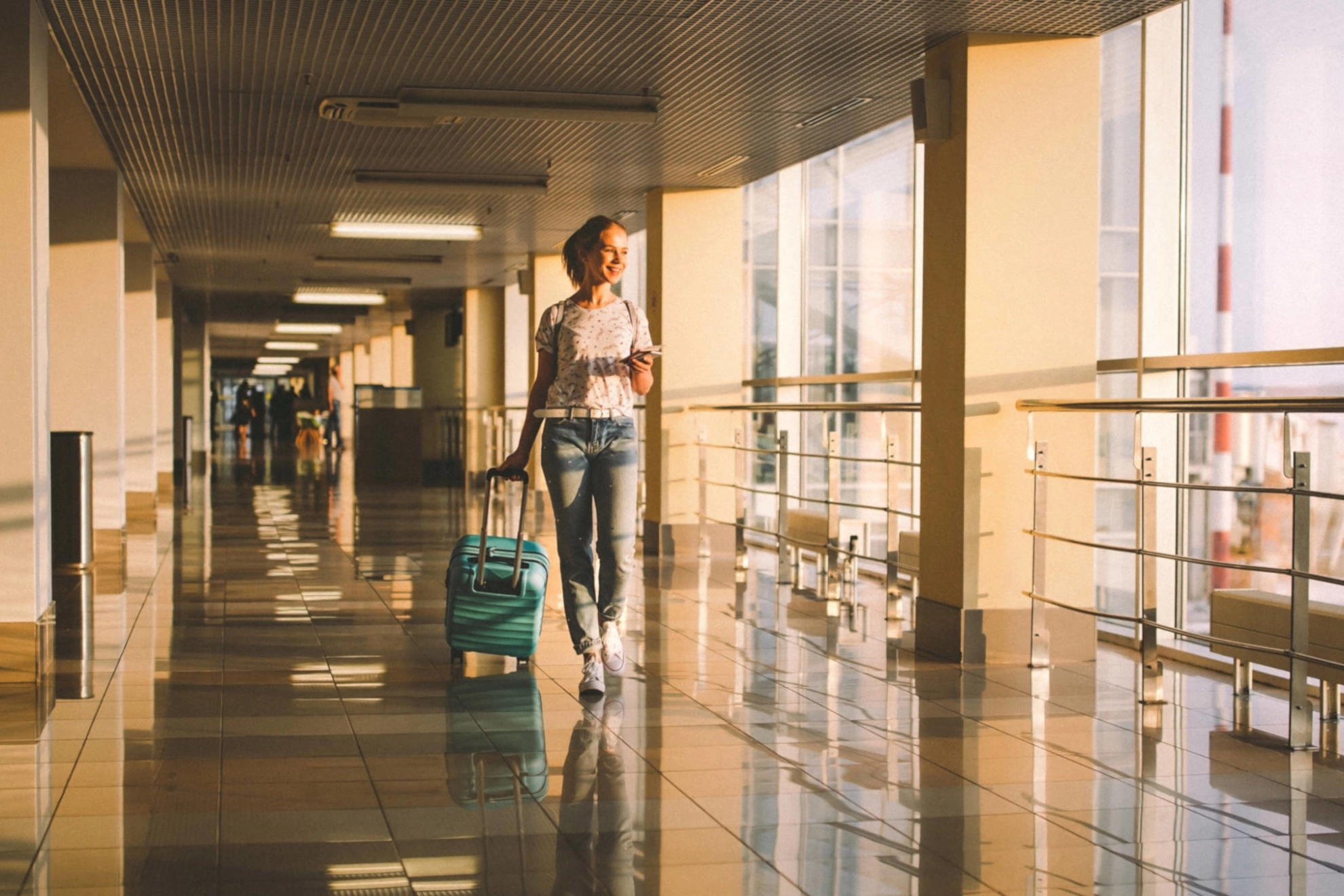 Eine junge Frau mit Rollkoffer geht durch einen Flur in einem Flughafen.